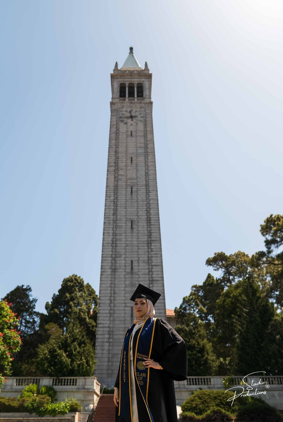 Graduate posing in cap and gown in front of the UC Berkeley Campanile