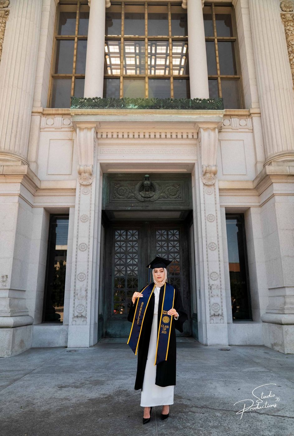 Graduate in cap and gown posing at the entrance of a campus building
