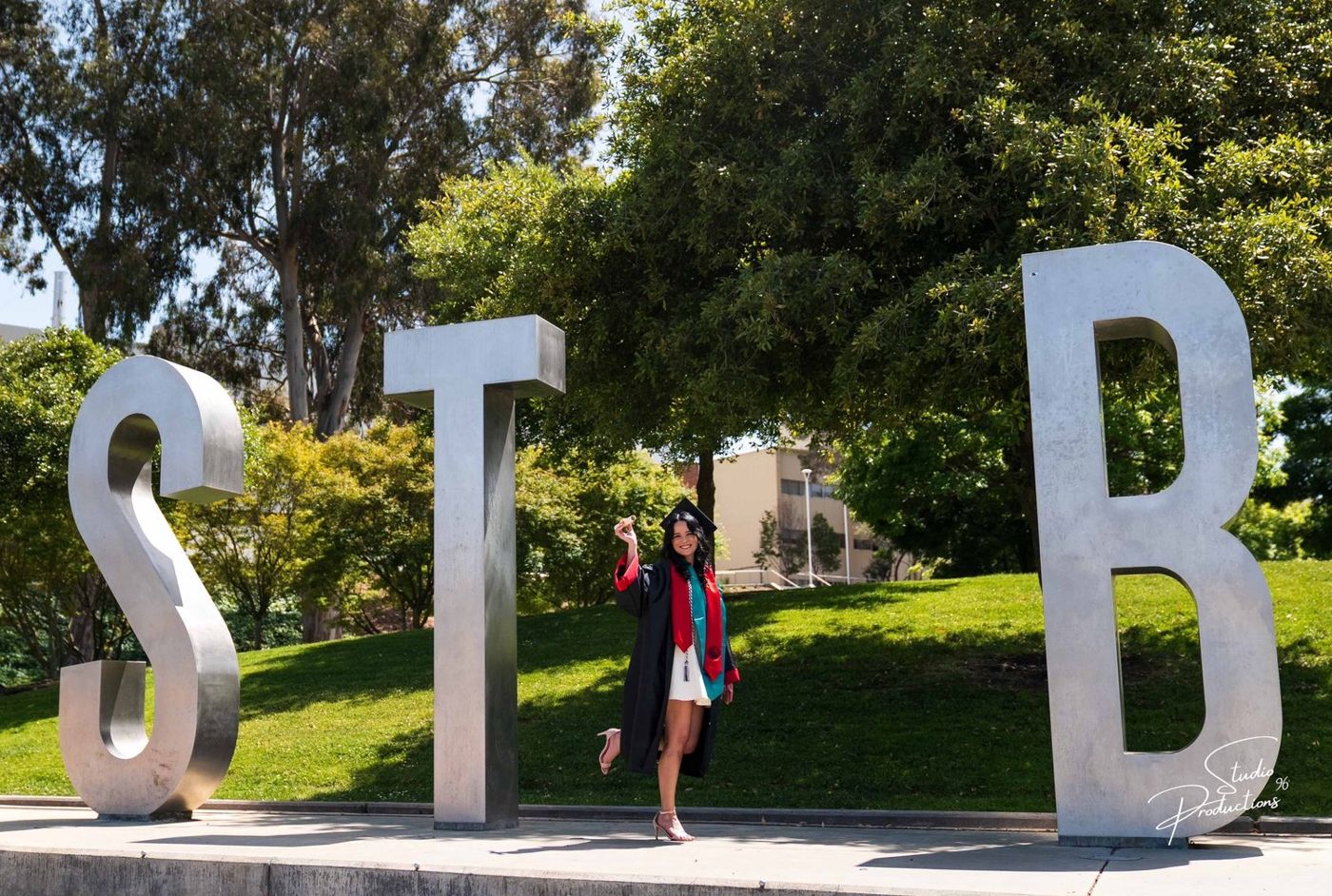 Graduate in a white dress and sash walking past large sculptural letters