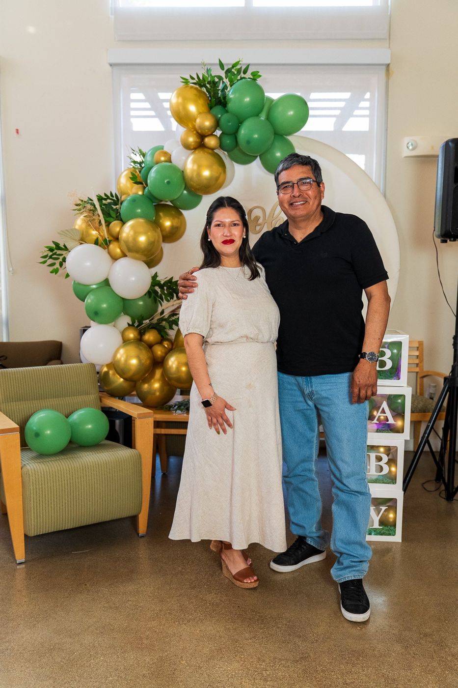 Mom-to-be posing with a guest in front of a green and gold balloon arch