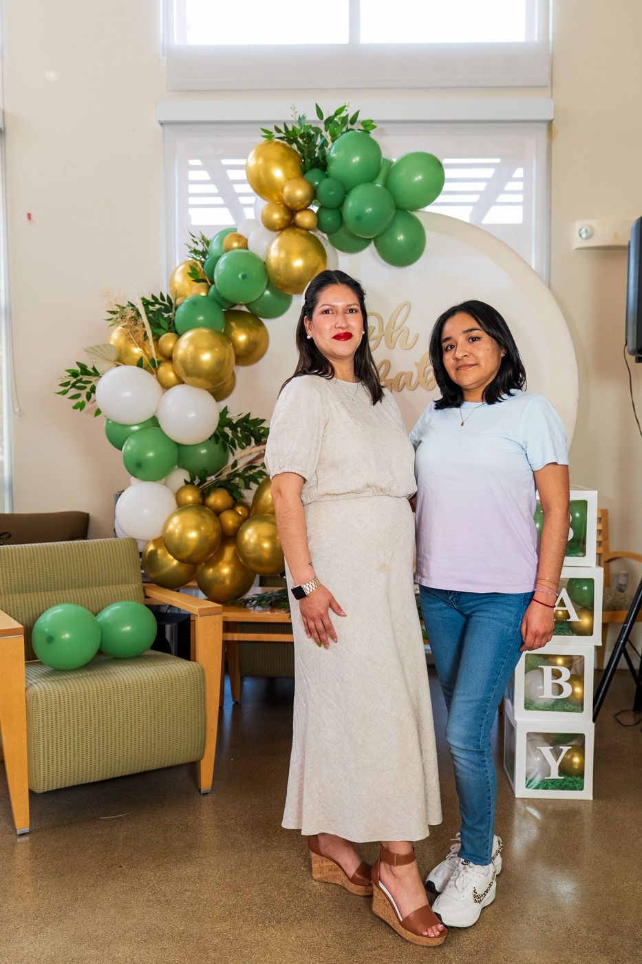Mom-to-be posing with a young guest in front of the balloon arch