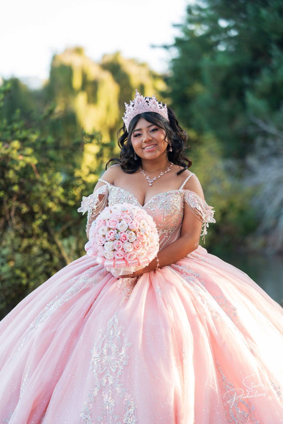 Quinceañera in her tiara, smiling among the garden trees