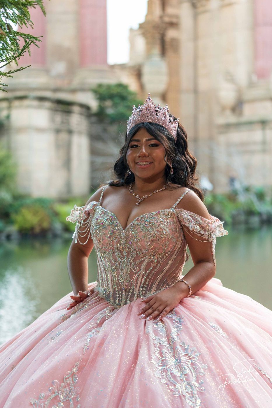 Quinceañera seated by the lagoon, smiling at the camera