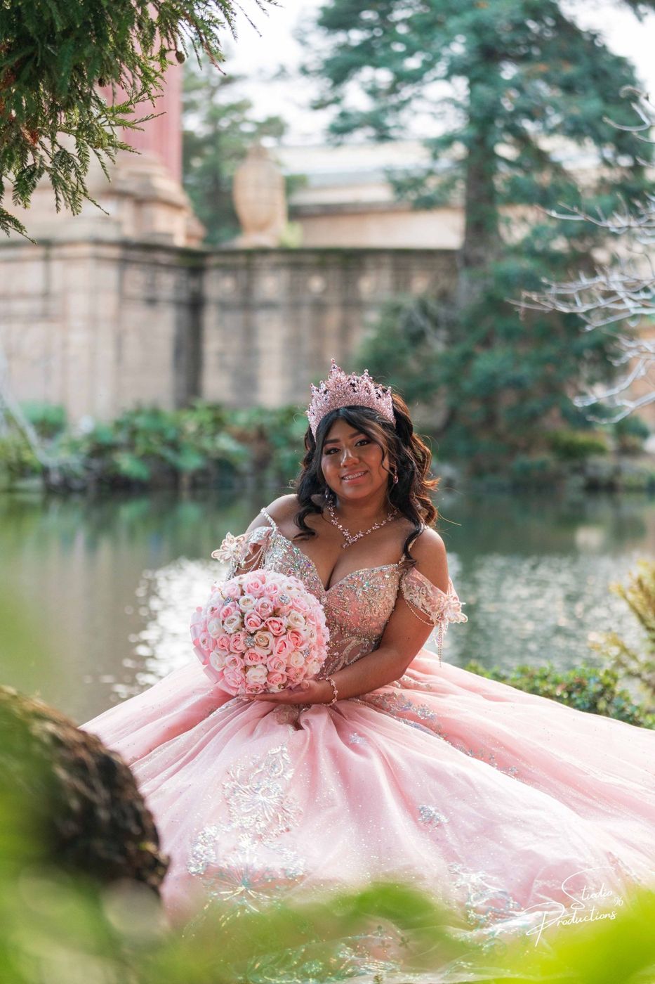 Quinceañera standing among the garden trees, holding her bouquet