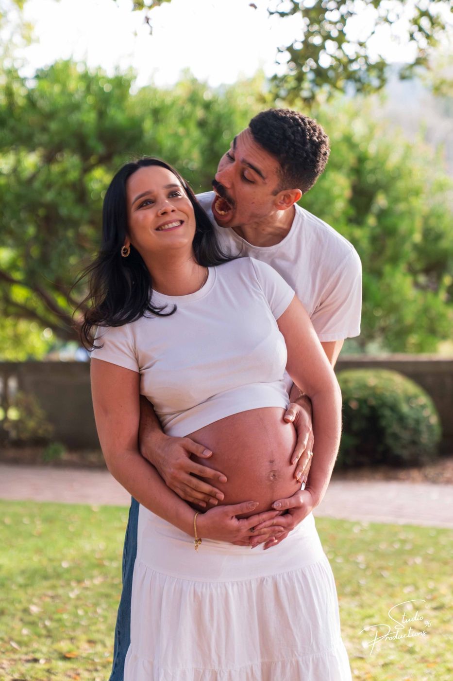 Expecting couple laughing together, husband nuzzling his wife's cheek, hand on her belly