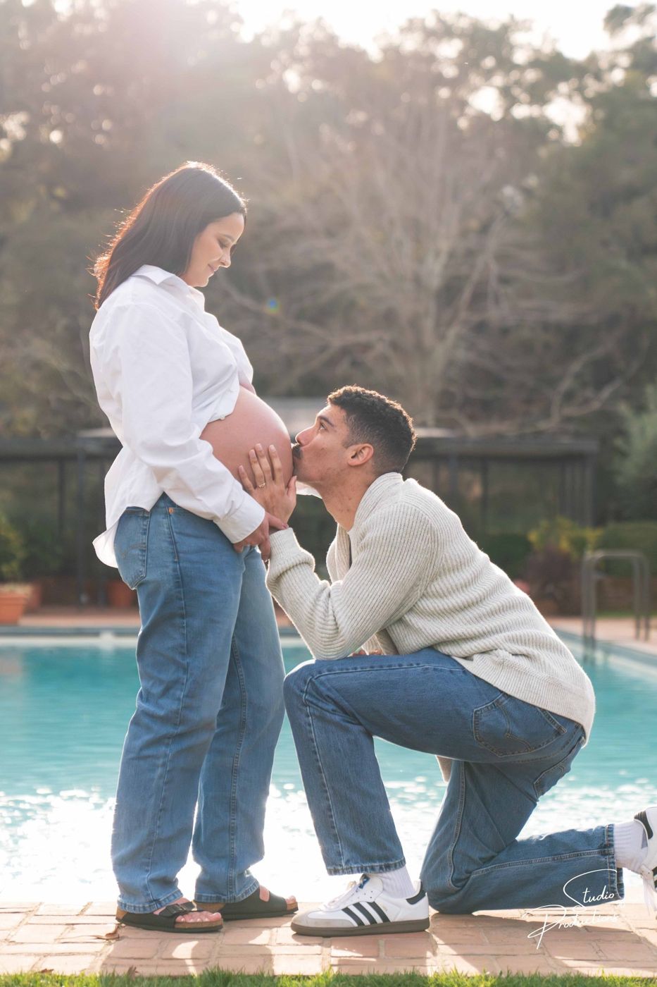 Husband kneeling to kiss his wife's belly poolside