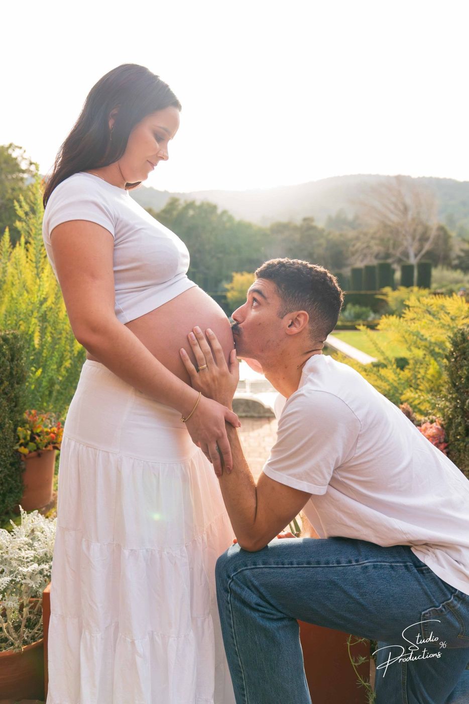 Husband kneeling to kiss his wife's belly near flowering plants