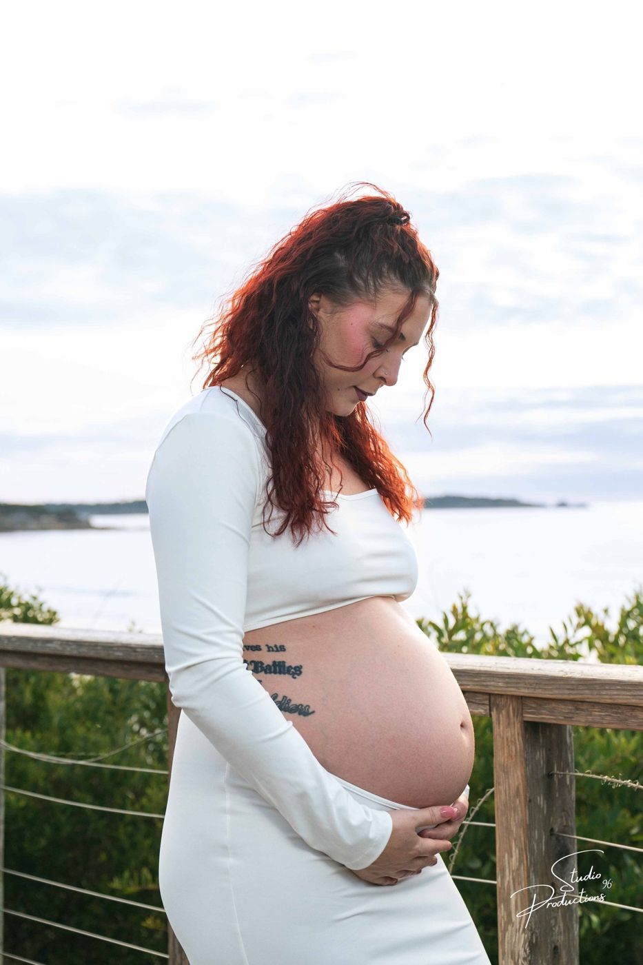 Expecting mother standing at a waterfront railing, hand on her belly