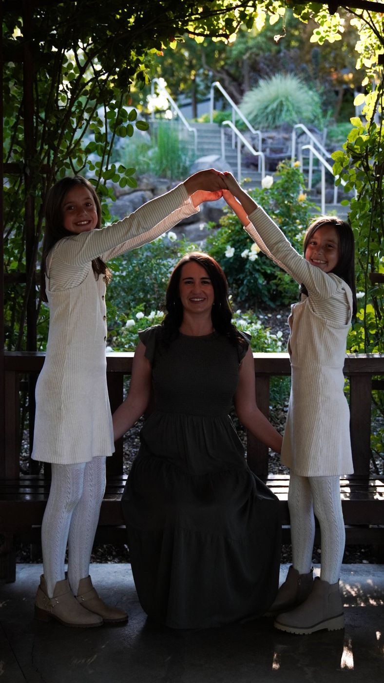 Mother and her two daughters forming a heart shape with their arms beneath a garden arbor