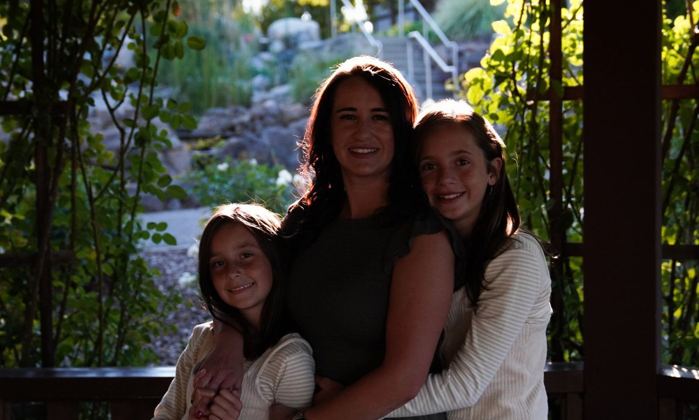 Mother embracing her two daughters beneath a garden pergola