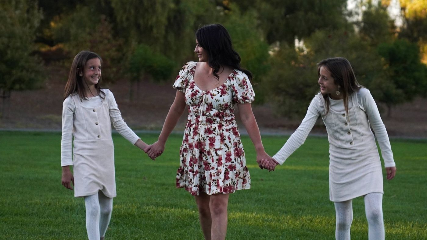 Mother and her two daughters walking hand in hand across the lawn