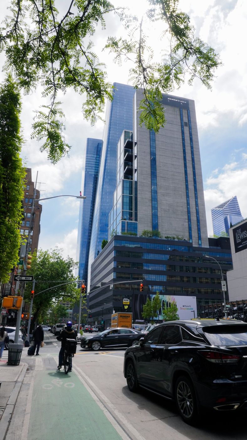 A glass Manhattan skyscraper rising above a tree-lined street