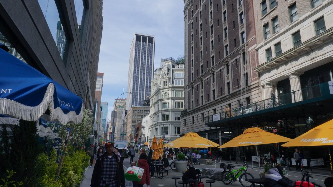A Manhattan street lined with shops, awnings, and pedestrians