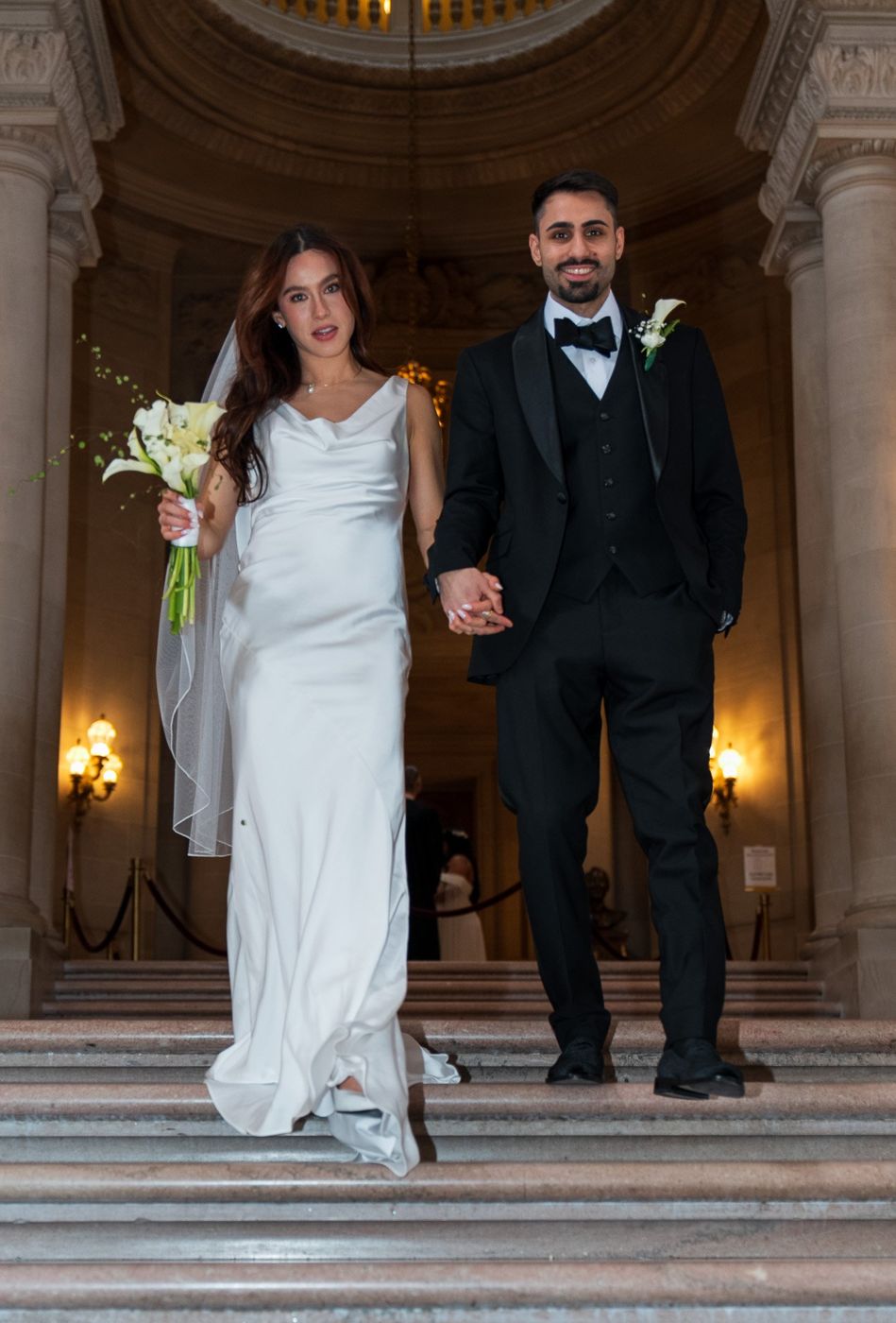 The couple arriving arm in arm at the top of the grand staircase