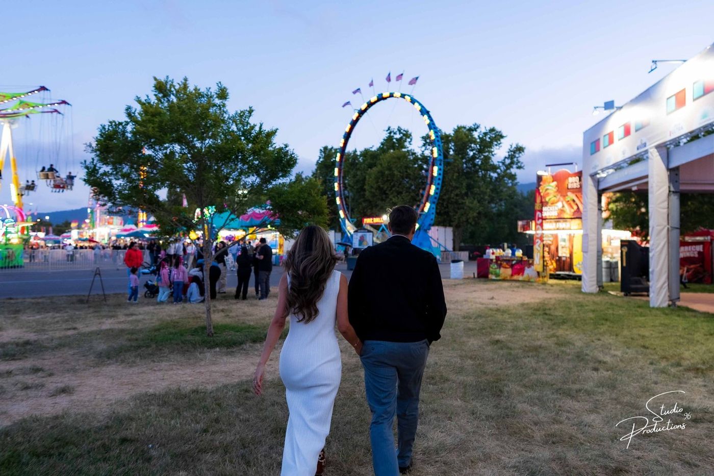 Wide shot of the couple walking away through the lit fairgrounds