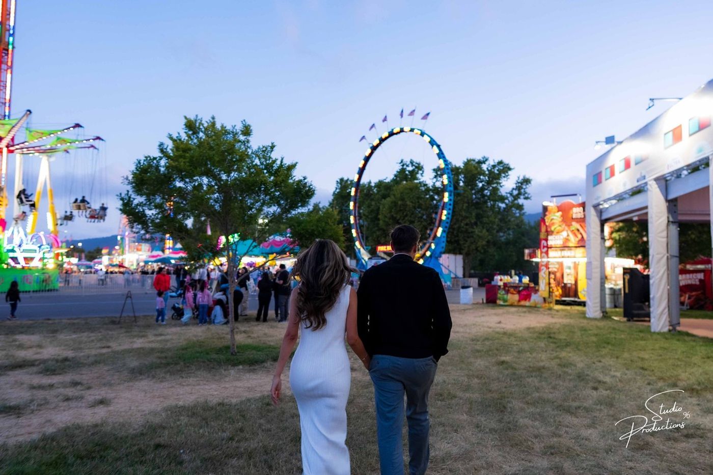 The couple walking together through the lit fairgrounds at dusk