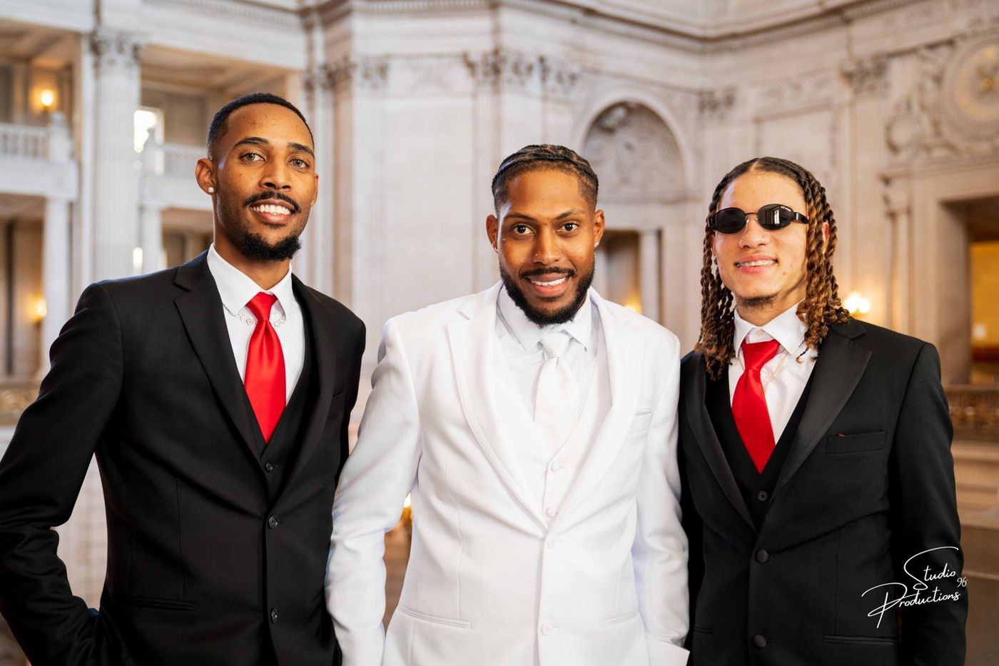 Portrait of the groom and two groomsmen in dark suits with red ties