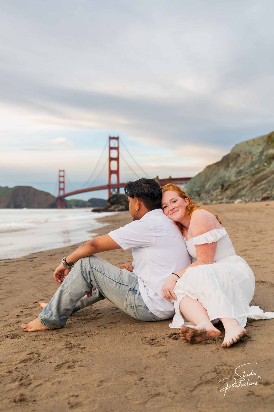 Couple walking hand in hand on the beach with the bridge behind them